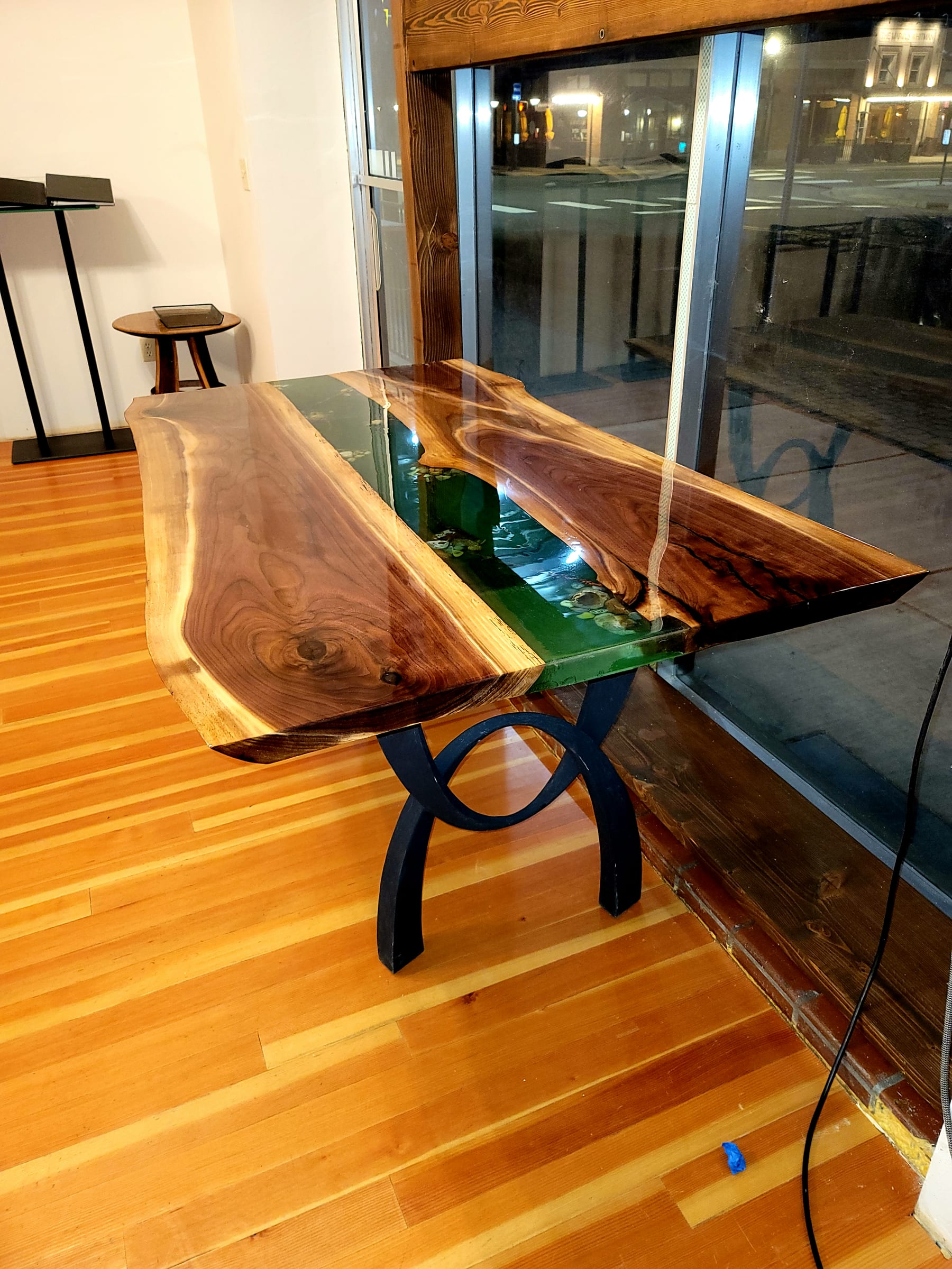 Walnut live-edge river table with deep green resin on a curved black steel base, by Ray Sample